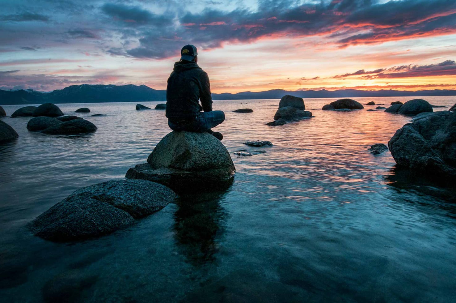 Person sitzt auf Stein im Wasser bei Sonnenaufgang